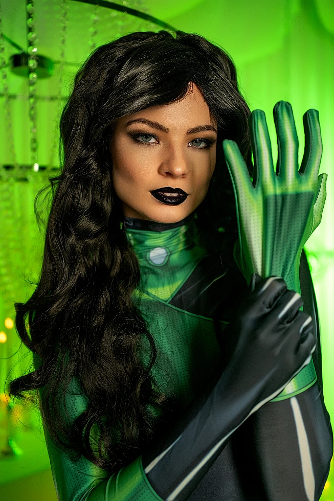 Shego cosplay close portrait, raised green glove, focused gaze, emerald background
