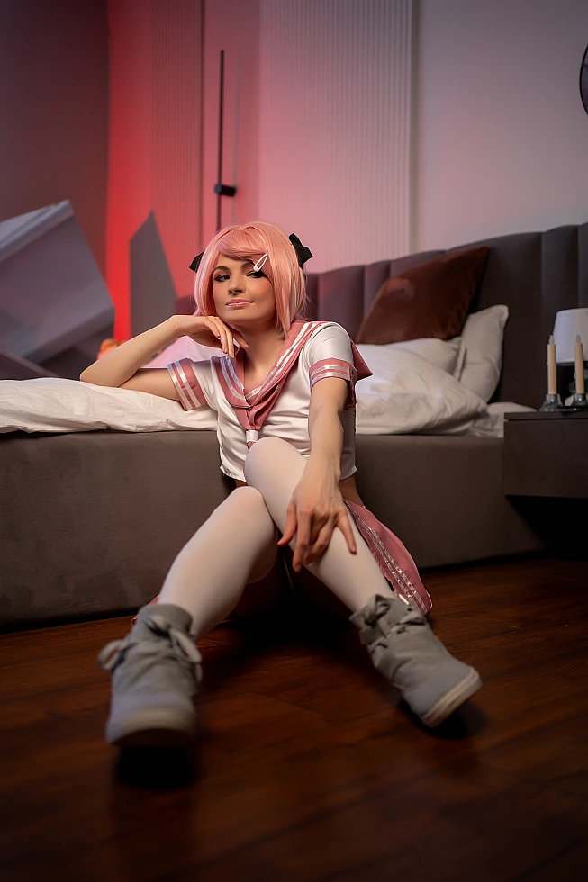 Astolfo trap cosplay sitting on floor with extended legs in pink school uniform and white thigh-high socks