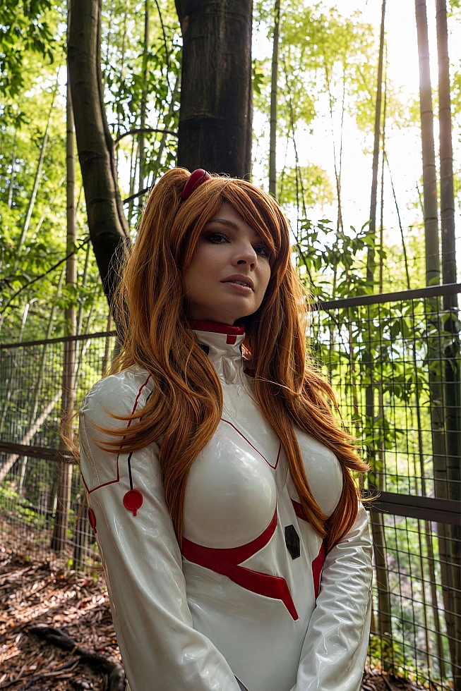 Asuka Langley cosplay portrait in a white Rebuild plugsuit with orange twin-tail wig standing in a bamboo grove