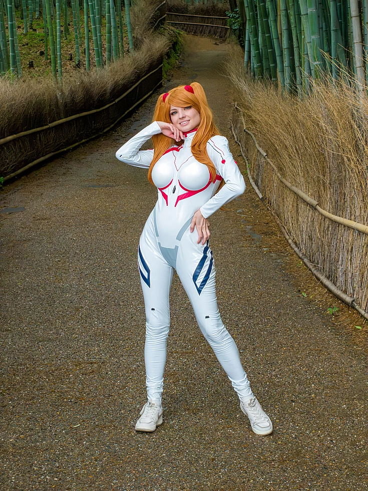Asuka Langley cosplay posing on a bamboo forest path in a white Rebuild plugsuit with orange twin-tail wig