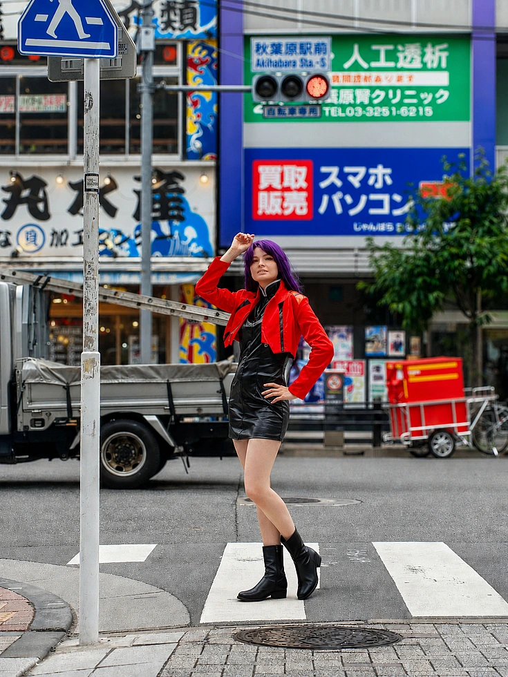 Full-body Misato Katsuragi cosplay posing on an Akihabara street crossing in a red jacket and black dress