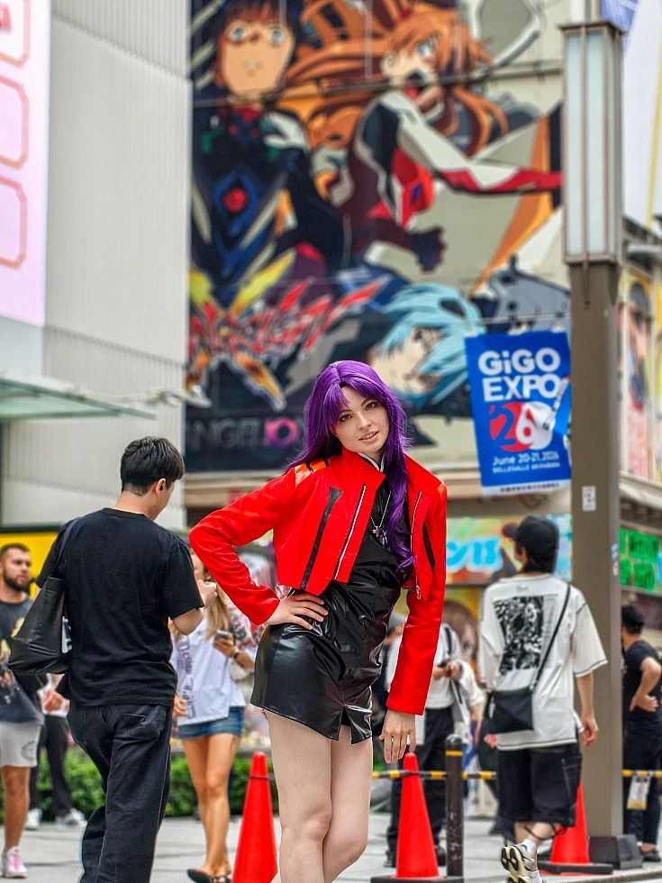 Misato Katsuragi cosplay posing in Akihabara near a large Evangelion mural with red jacket and purple hair