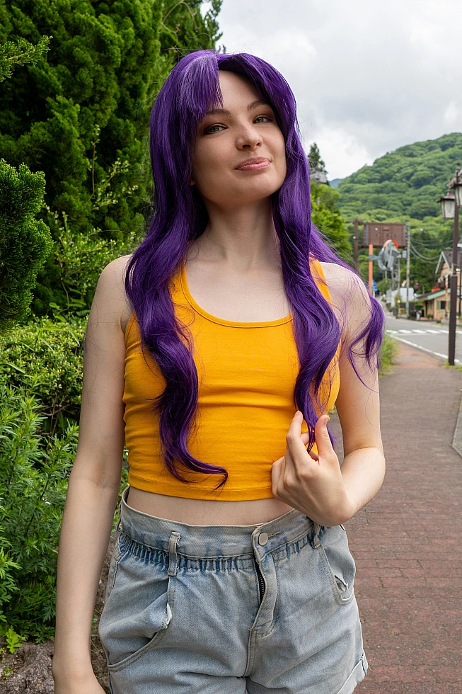 Misato Katsuragi casual cosplay with purple hair, yellow top and denim shorts standing on a quiet mountain town street