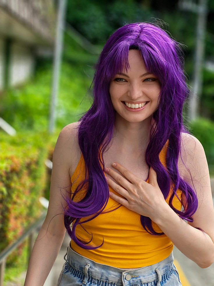 Misato Katsuragi casual cosplay smiling outdoors with long purple hair, yellow top and green background