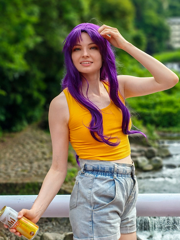 Misato Katsuragi casual cosplay standing by a riverside railing with purple hair, yellow top and denim shorts