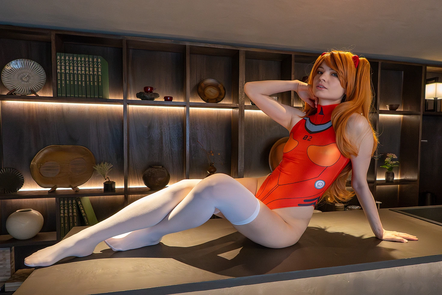 Asuka Langley cosplay reclining in a Japanese inn lounge with red swimsuit, white stockings and orange twin-tail wig