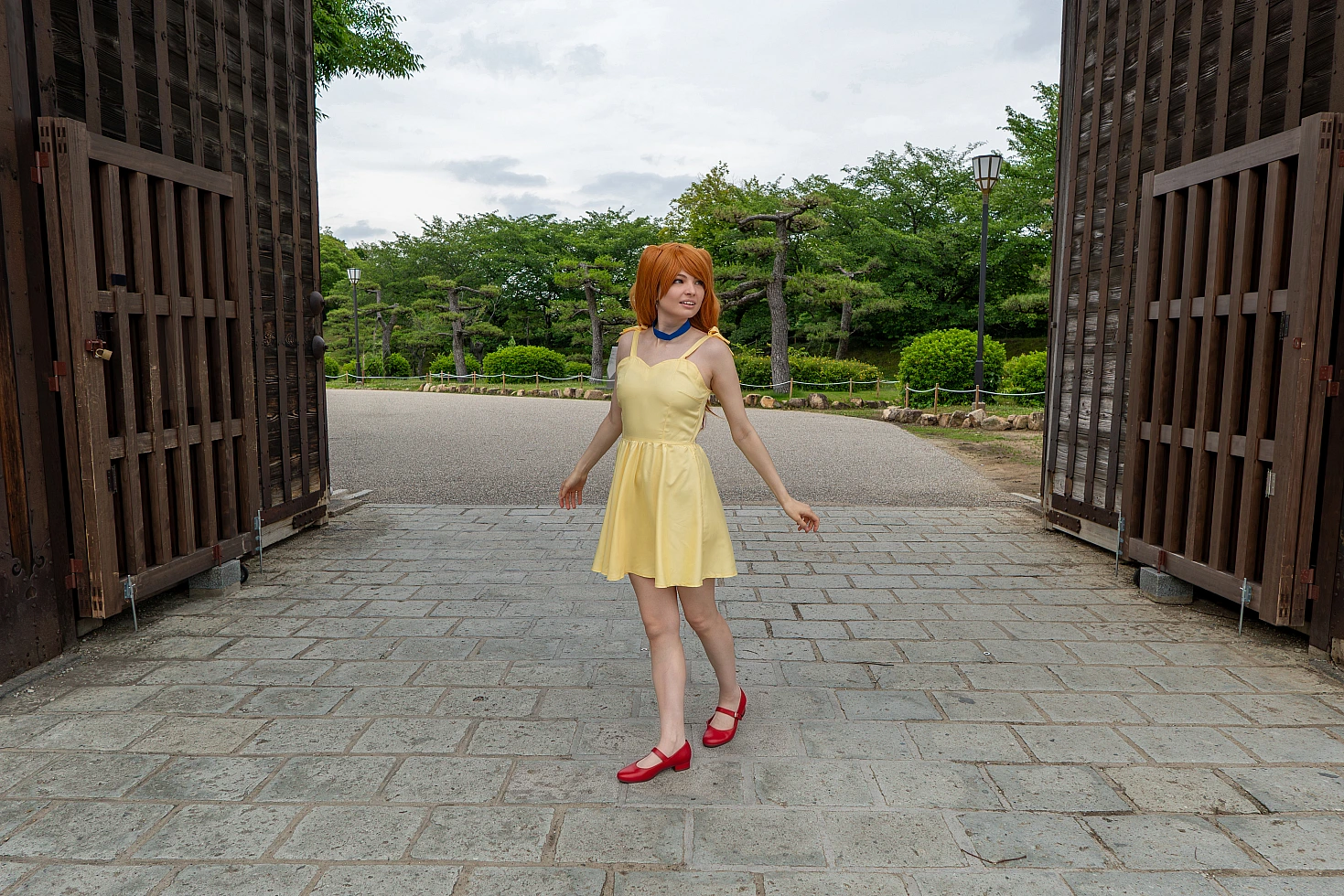 Full-body Asuka Langley cosplay walking through a Japanese castle gate in a yellow summer dress and red shoes